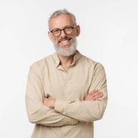 Smart caucasian mature middle-aged freelancer man in beige shirt wearing glasses looking at camera with arms crossed isolated in white background